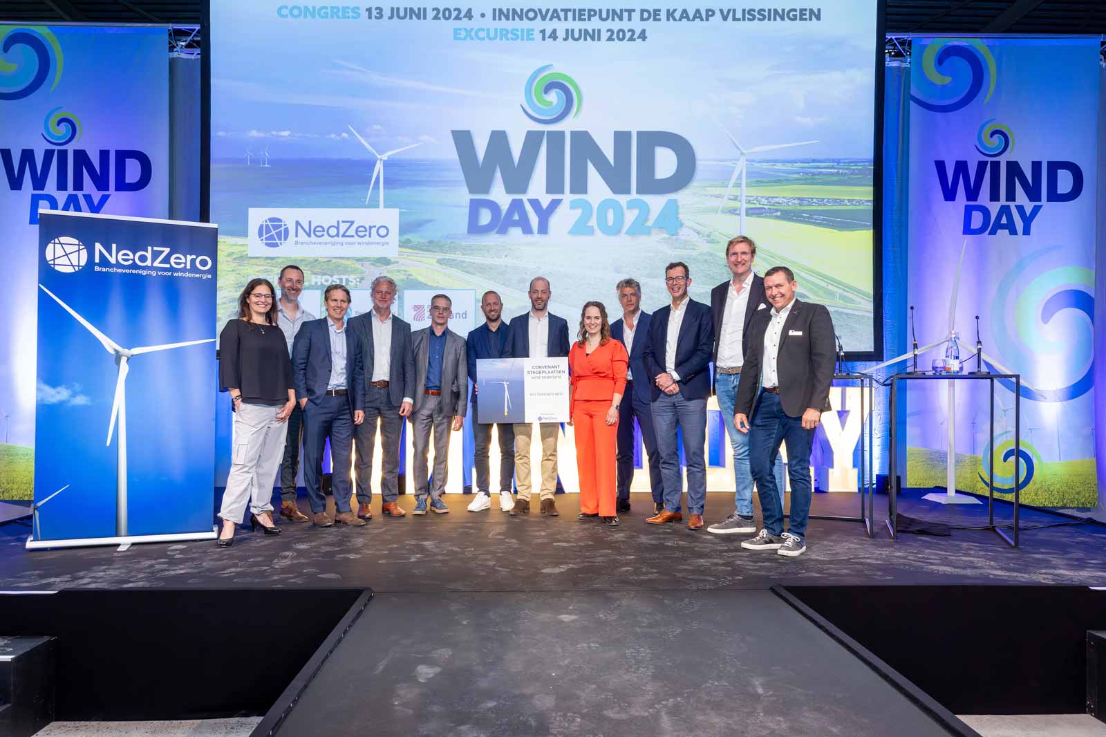 A group of professionals at a conference for Wind Day 2024, with a large screen behind them showcasing wind energy themes.