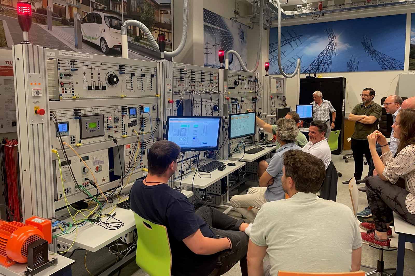 A group of people engaged in a practical session with control panels and computer monitors in a lab.
