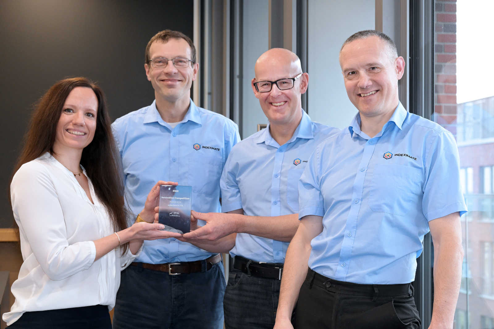 A group of four individuals, two men in blue shirts and a woman in a white shirt, holding an award together.