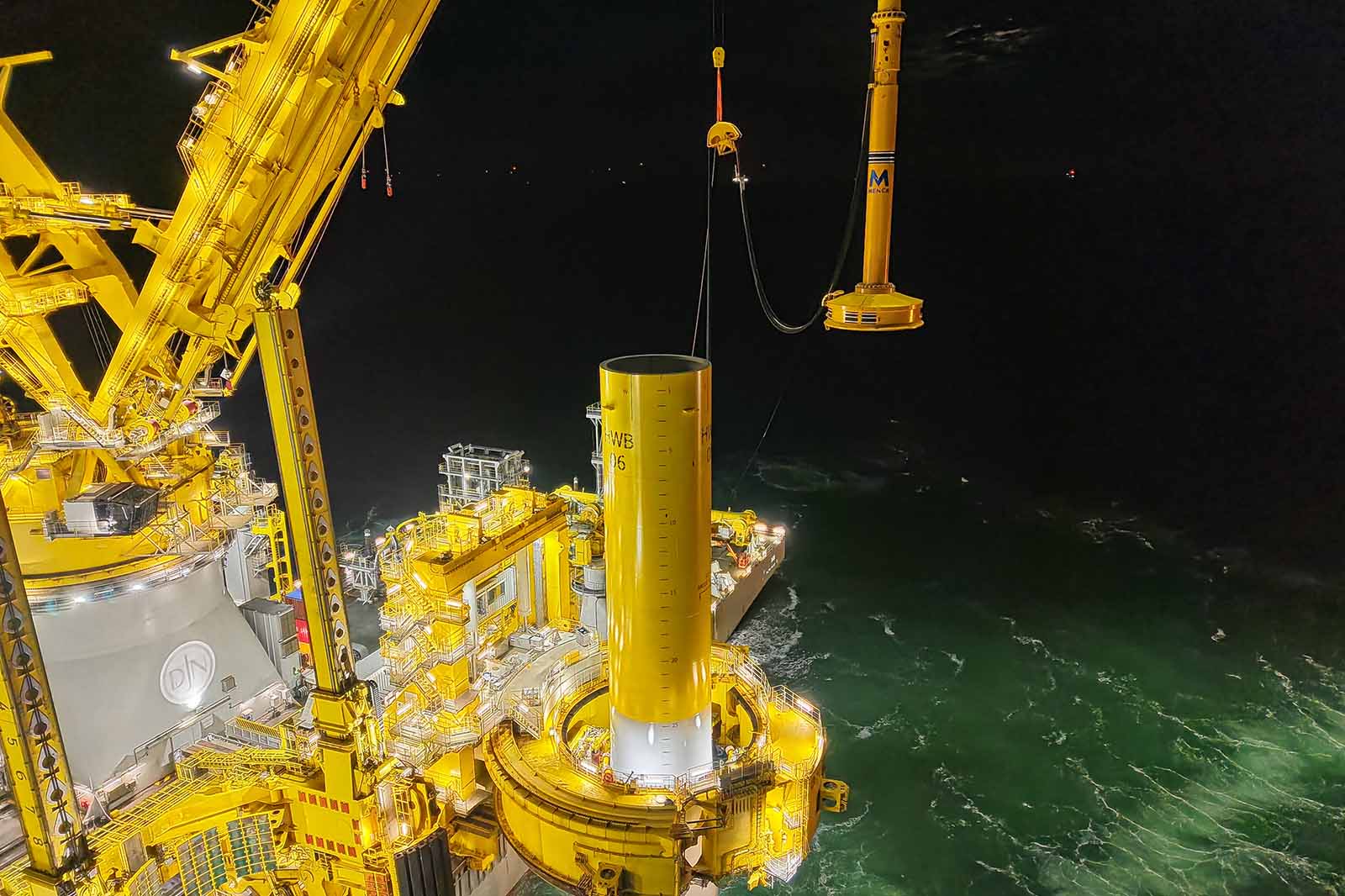A yellow offshore platform and crane operating at night over the illuminated sea surface.